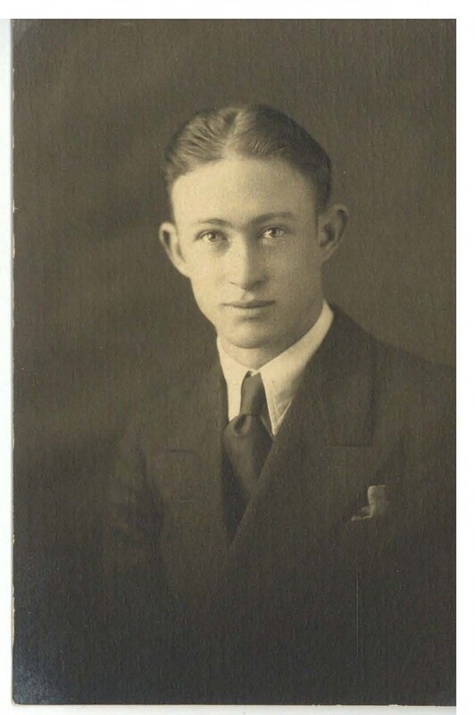 a black and white portrait of a teenaged boy. His neatly combed hair is parted down the center, and he is wearing a suit.